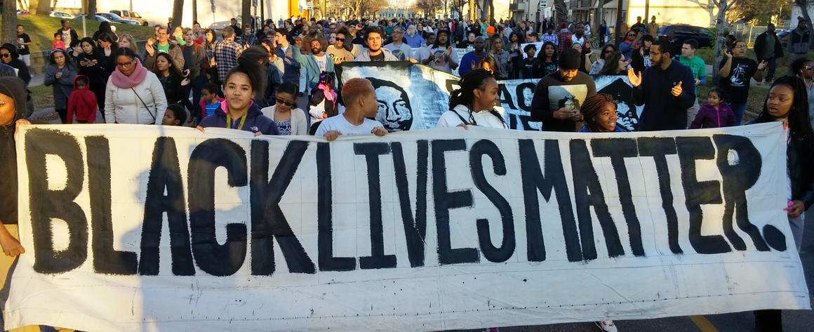 A group of protestors marching behind a banner that reads "Black Lives Matter"