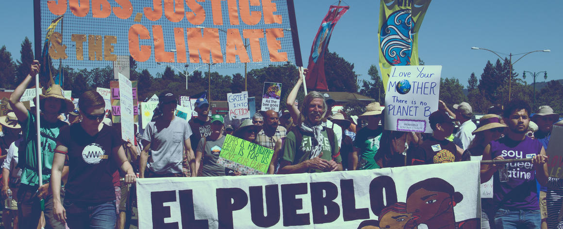 Signs carried by marchers reading "El Pueblo Unido" and "United for Jobs Justice and Climate"